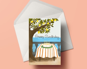May include: A birthday card with a lemon tree illustration. The card features a white cake with lit candles on a striped table with a blue ocean in the background. The text "Happy Birthday" is written in black cursive.
