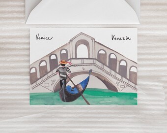 May include: A watercolor illustration of a gondola in Venice, Italy. The gondola is in the water under a bridge with a gondolier standing in the back. The text "Venice" and "Venezia" are written on the card.