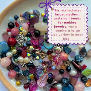 May include: A collection of assorted beads in various shapes, sizes, and colors, including pink, purple, blue, and metallic tones. A white scalloped sign with a purple bow contains the text: this mix includes large, medium, and small beads for making jewelry. you will receive a large size variety in each bag!