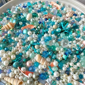 Può includere: Una collezione di perline assortite nelle tonalità turchese, verde acqua, azzurro e bianco, mescolate a piccole conchiglie e ciondoli a forma di corallo. L'assortimento comprende perline rotonde, sfaccettate e perlate di varie dimensioni.