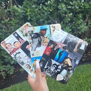 May include: Three rectangular art prints featuring collages of musicians. The prints showcase images of Tyler, the Creator, Mac Miller, and Michael Jackson. The prints are held in a hand against a backdrop of green foliage.