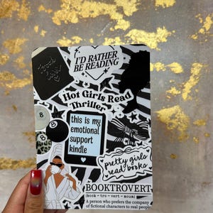 May include: A black and white sticker sheet with various text and graphic designs. Text includes "I'd Rather Be Reading", "Hot Girls Read Thriller", and "Booktrovert". Graphics include a silhouette, bow, and a person in a robe.