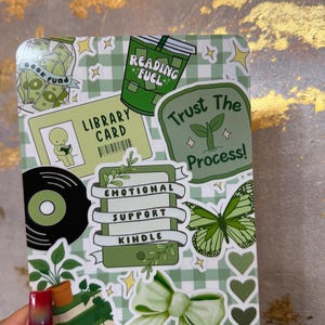 May include: A green and white sticker sheet with various illustrations and text. Designs include a library card, a vinyl record, a butterfly, hearts, and the phrases "Reading Fuel" and "Trust The Process!"