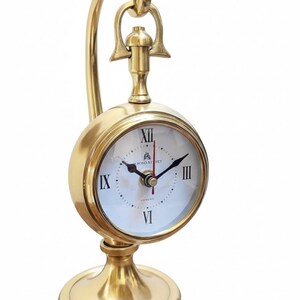 May include: A gold-colored desk clock with a round face and a curved handle. The clock face has Roman numerals and the words "Bond Street London". The clock sits on a round base.