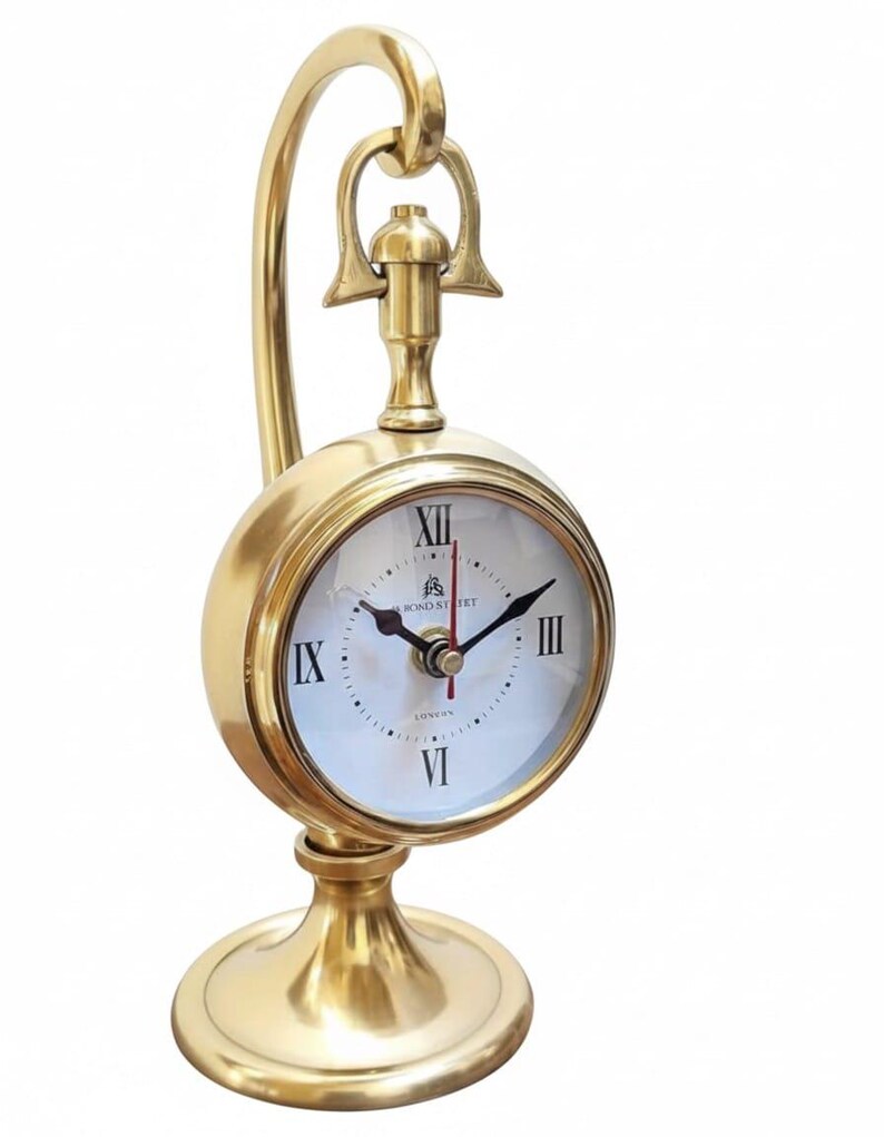 May include: A gold-colored desk clock with a round face and a curved handle. The clock face has Roman numerals and the words "Bond Street London". The clock sits on a round base.