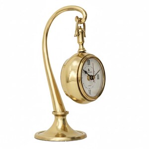 May include: A gold-colored, hanging desk clock with a white face and black Roman numerals. The clock is suspended from a curved stand with a round base. The clock face has the brand name "WESTMINSTER" printed on it.