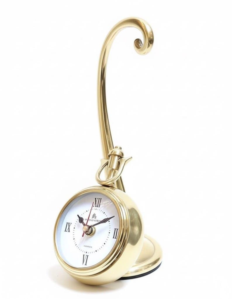 May include: A gold-colored desk clock with a round face and Roman numeral hour markers. The clock has a curved, ornate stand and a small base. The clock face is white with black hands and the brand name "London" is visible.