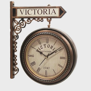 May include: A double-sided, antique-style clock with the word "VICTORIA" on a sign above the clock face. The clock face has Roman numerals and the words "VICTORIA STATION" and "1747". The clock is bronze-colored.