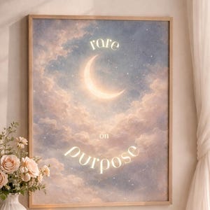 Puede incluir: Una impresión artística enmarcada con un diseño celestial. Presenta una luna creciente y las palabras "rare on purpose" sobre un cielo nublado en colores pastel. Un jarrón con flores y una vela encendida están sobre una mesa cercana.