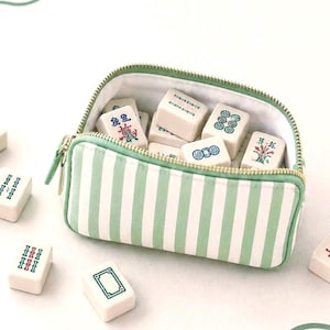 Coastal inspired  mahjong tile bag in sage green and ivory stripes resting on an ivory mahjong mat with tiles