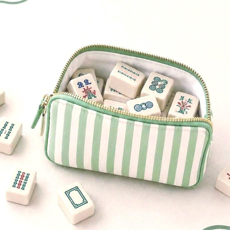 Coastal inspired  mahjong tile bag in sage green and ivory stripes resting on an ivory mahjong mat with tiles