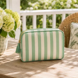 May include: A rectangular zippered pouch featuring vertical mint green and white stripes. The bag has a gold-toned zipper closure accented with a matching mint green fabric tassel attached to the pull tab, providing a structured storage solution.