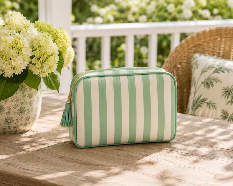 May include: A rectangular zippered pouch featuring vertical mint green and white stripes. The bag has a gold-toned zipper closure accented with a matching mint green fabric tassel attached to the pull tab, providing a structured storage solution.