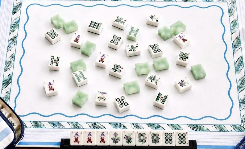 coastal inspired mahjong mat featuring custom ivory stitching, blue and while pinstripe boarder,  palm leaves and a bold coastal blue wavy line- all to lead you to a clean center for game night