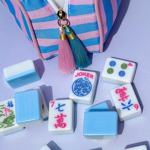 The mahjong tile bag with various mahjong tiles with blue, pink, and green engraved faces. Melamine Mahjong Tiles set