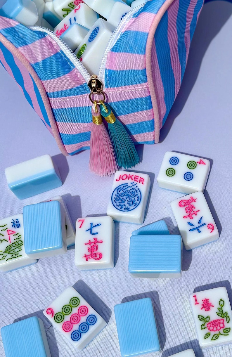 The mahjong tile bag with various mahjong tiles with blue, pink, and green engraved faces. Melamine Mahjong Tiles set