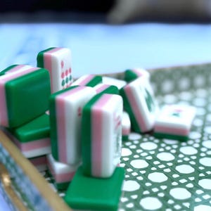 A close-up, slightly blurry shot of several green and pink mahjong tiles stacked and scattered on a green and white patterned tray.