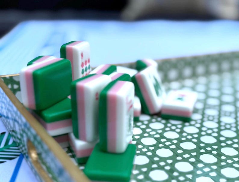 A close-up, slightly blurry shot of several green and pink mahjong tiles stacked and scattered on a green and white patterned tray.