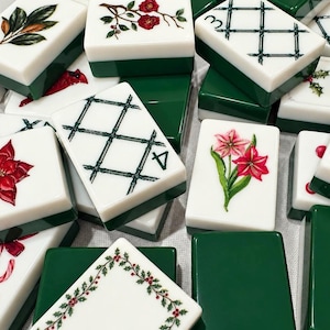 May include: A collection of white and dark green mahjong tiles featuring various holiday-themed illustrations including red poinsettias, candy canes, holly berries, floral sprigs, and black bamboo grid patterns with the number four visible.