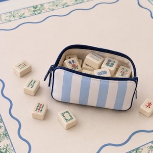 Coastal mahjong tile bag in blue and ivory stripes resting on a blue and green mahjong mat with tiles.