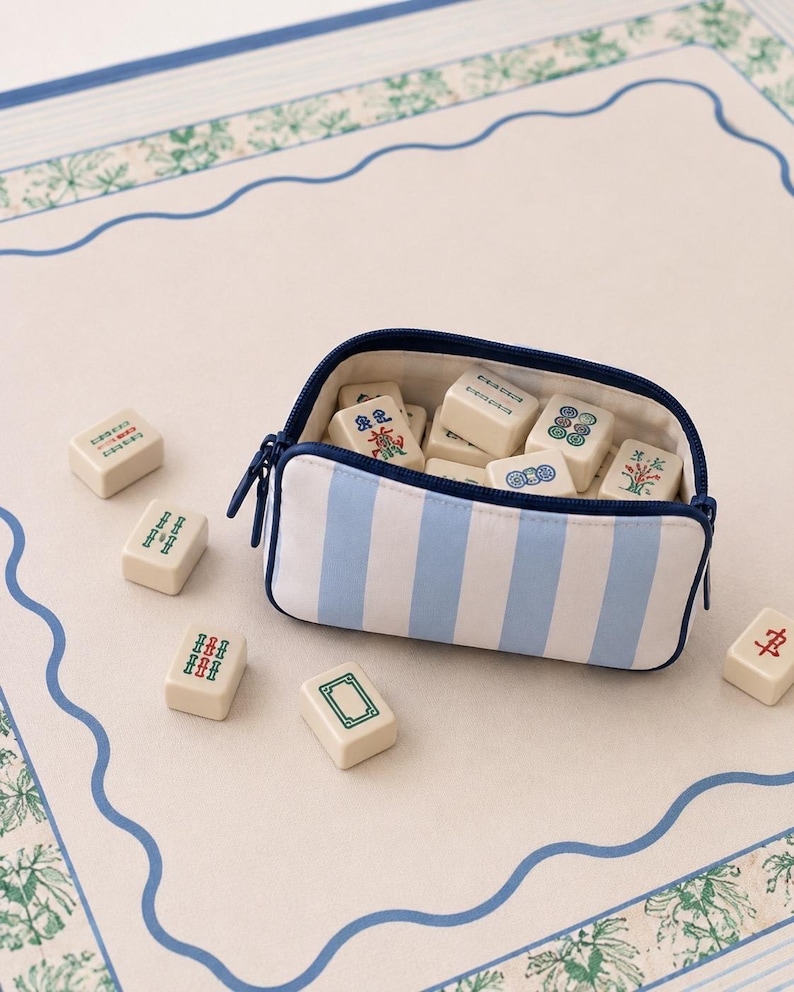Coastal mahjong tile bag in blue and ivory stripes resting on a blue and green mahjong mat with tiles.