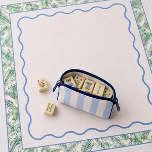 Coastal mahjong tile bag in blue and ivory stripes resting on a blue and green mahjong mat with tiles.