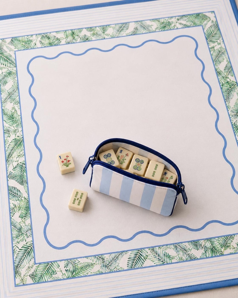 Coastal mahjong tile bag in blue and ivory stripes resting on a blue and green mahjong mat with tiles.