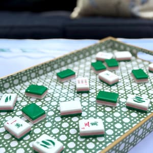 A collection of green and pink mahjong tiles with various symbols scattered across a green and white patterned tray.
