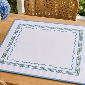 May include: A rectangular placemat featuring a white center bordered by a blue wavy line, a green and white palm leaf patterned frame, and an outer border of thin blue lines on a white background, finished with a solid light blue edge.