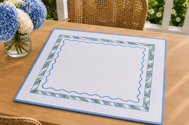 May include: A rectangular placemat featuring a white center bordered by a blue wavy line, a green and white palm leaf patterned frame, and an outer border of thin blue lines on a white background, finished with a solid light blue edge.