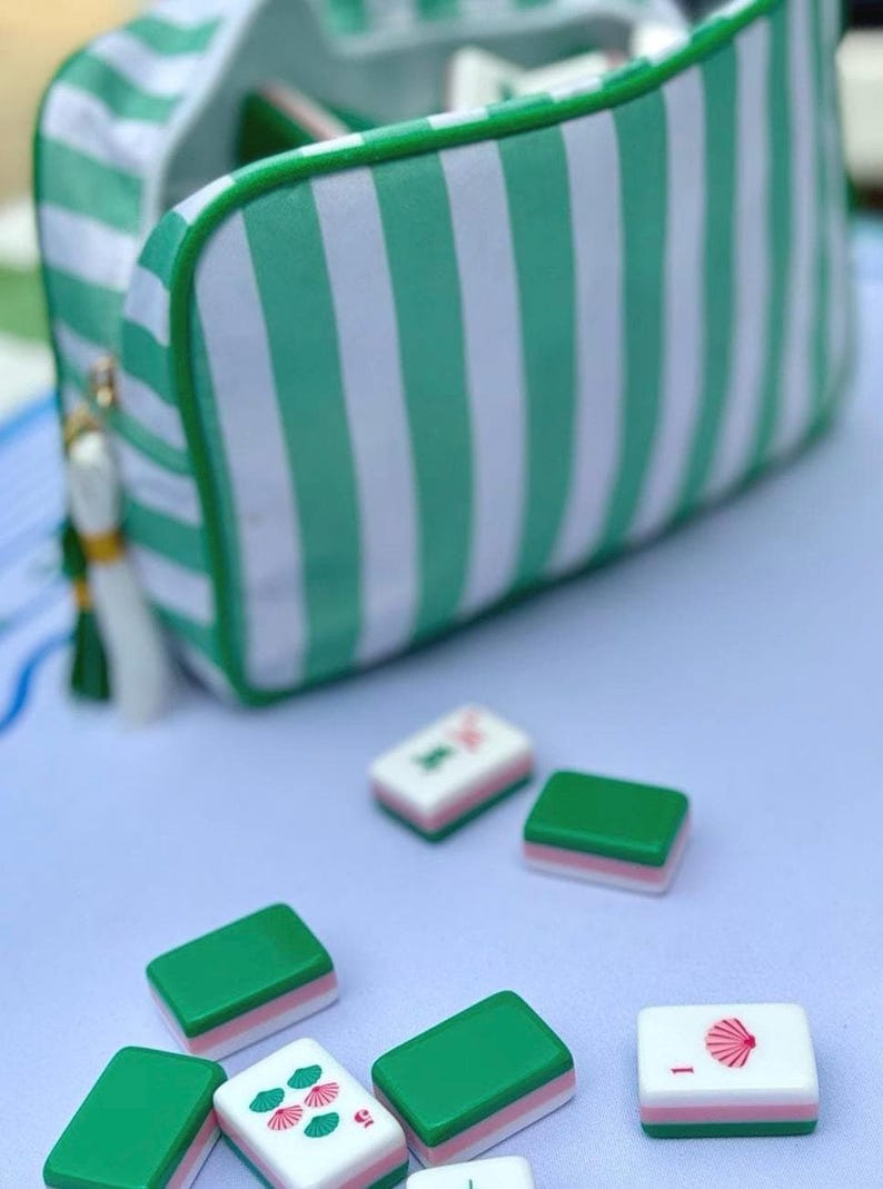May include: A green and white striped zippered pouch with a tassel zipper pull, accompanied by several rectangular mahjong tiles. The tiles feature green, white, and pink layers, with some displaying red shell icons and the number one.