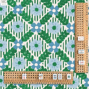 May include: A patterned fabric featuring light blue flowers with green centers and dark green leafy sprigs over a white background with vertical green stripes. Two woven rattan mahjong tile racks are positioned on the fabric surface.
