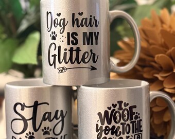 May include: Three silver glitter mugs stacked on top of each other. The top mug says "Dog hair is my Glitter". The middle mug says "Stay Pawsitive". The bottom mug says "I Woof You to the Moon and Back".