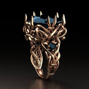 May include: A rose gold ring featuring an intricate, interwoven metal band with multiple pointed prongs. The setting holds a large, dark blue central gemstone, accented by smaller, round, dark blue stones embedded within the metal structure.