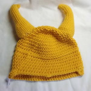 May include: A yellow crocheted hat with two horns. The hat is made with a single crochet stitch and has a simple design.