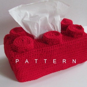 Op de afbeelding: Rode gehaakte tissueboxhoes in de vorm van een Lego-steen met het woord "PATTERN" erop gedrukt.