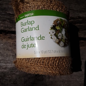 Może przedstawiać: Rolka brązowej girlandy jutowej, o szerokości 5 cali i długości 10 jardów, z zieloną etykietą z napisem "Simplestyle Burlap Garland Guirlande de jute 5 in x 10 yd (12.7 cm x 9.14 m)".