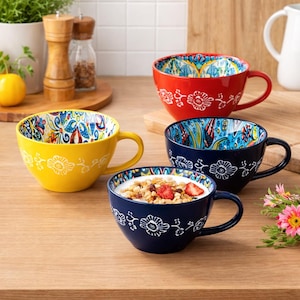 May include: Four ceramic soup mugs in red, yellow, and blue with floral patterns. The mugs have a large handle and a decorative floral design on the outside. One mug is filled with granola and strawberries.