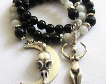 May include: A black and white beaded necklace with a silver crescent moon pendant featuring a bird skull and a silver female figure pendant.