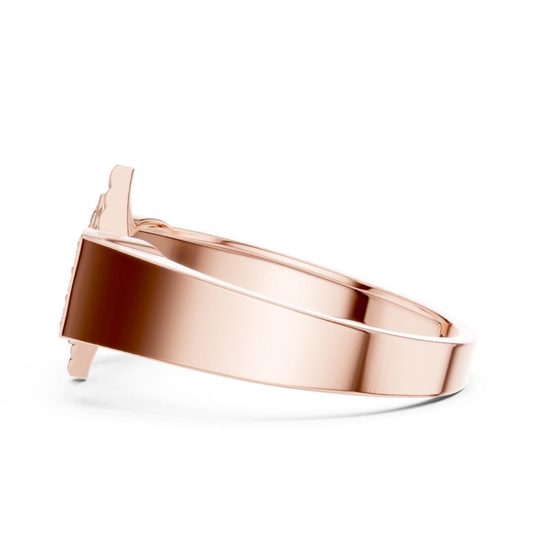 May include: Rose gold ring with a minimalist design. The ring features a smooth, polished band and a decorative element on the top. The ring is shown from a side angle, highlighting its sleek and modern aesthetic. This piece of jewelry is suitable for everyday wear.