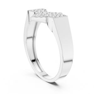May include: A silver ring with a rectangular top, adorned with small, sparkling stones. The band curves smoothly, creating a modern and elegant design. The ring is shown against a white background, highlighting its polished finish.