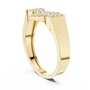May include: A gold ring with a geometric design. The ring features a rectangular top with embedded small, clear stones. The band is a smooth, polished gold. The ring is set against a white background.