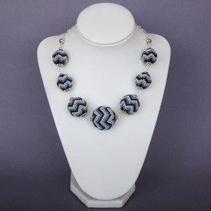 May include: A silver chain necklace with black and white chevron patterned beads. The beads are round and have a textured surface.