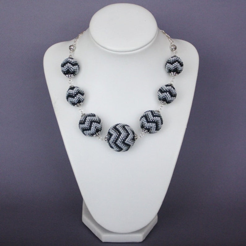 May include: A silver chain necklace with black and white chevron patterned beads. The beads are round and have a textured surface.
