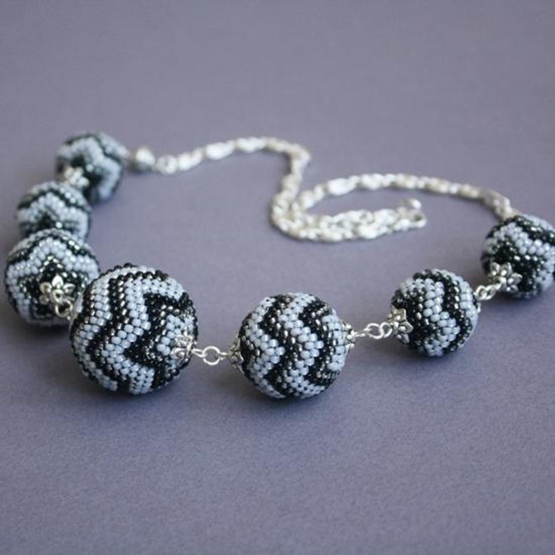 May include: A black and white beaded necklace with a chevron pattern. The necklace is made of large, round beads and has a silver chain.