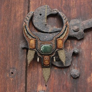 May include: A beaded necklace with a large green stone and amber accents. The necklace is hanging on a rusty metal hook.