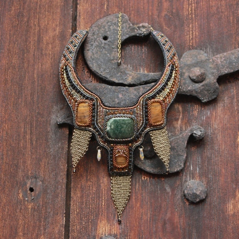 May include: A beaded necklace with a large green stone and amber accents. The necklace is hanging on a rusty metal hook.