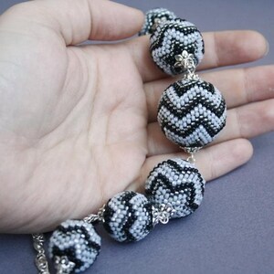 May include: A black and white beaded necklace with chevron patterned beads. The necklace is made of silver and black beads and is strung on a silver chain.