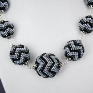 May include: A silver chain necklace with black and silver beaded balls. The beads have a chevron pattern.