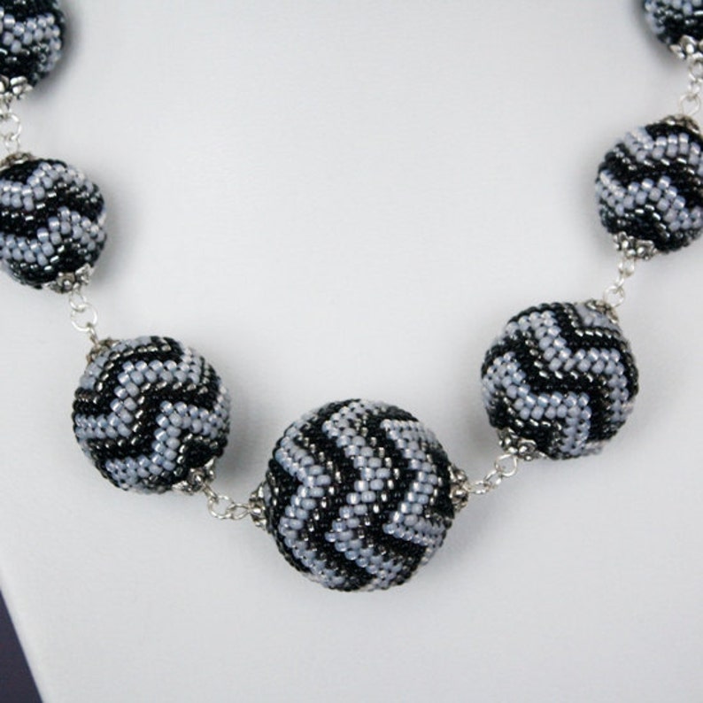 May include: A silver chain necklace with black and silver beaded balls. The beads have a chevron pattern.